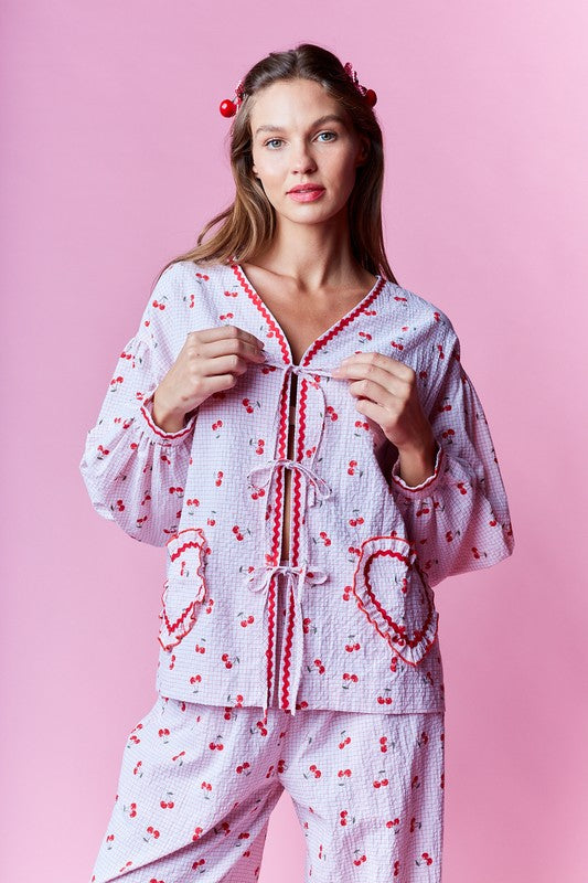 Women's cherry-print pajama set in pink, featuring a cozy top with heart pockets and matching pants.