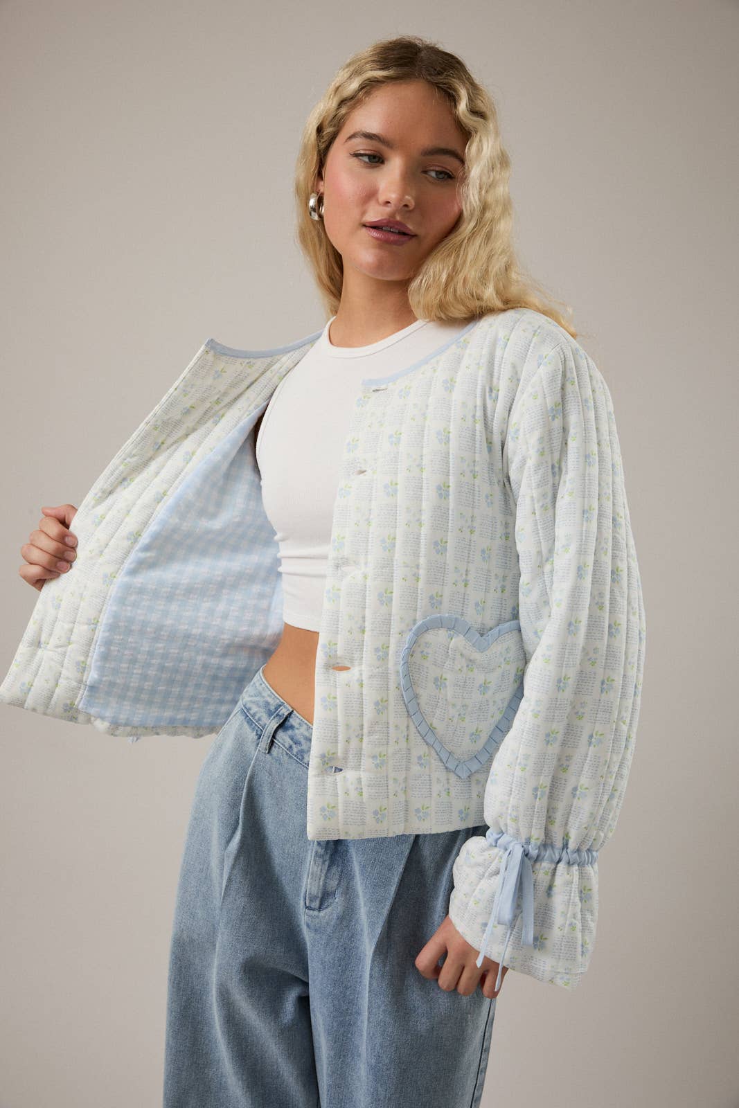Light blue quilted cardigan with heart pocket, floral pattern, and ruffled sleeves.