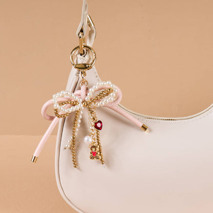 Chic beige handbag with pearl and gold charm bow detail, perfect for stylish outings.