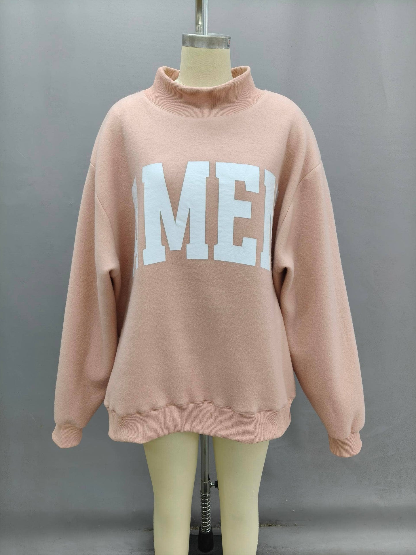 Oversized pink sweatshirt with white lettering, made from soft fleece material, featuring a cozy high collar.