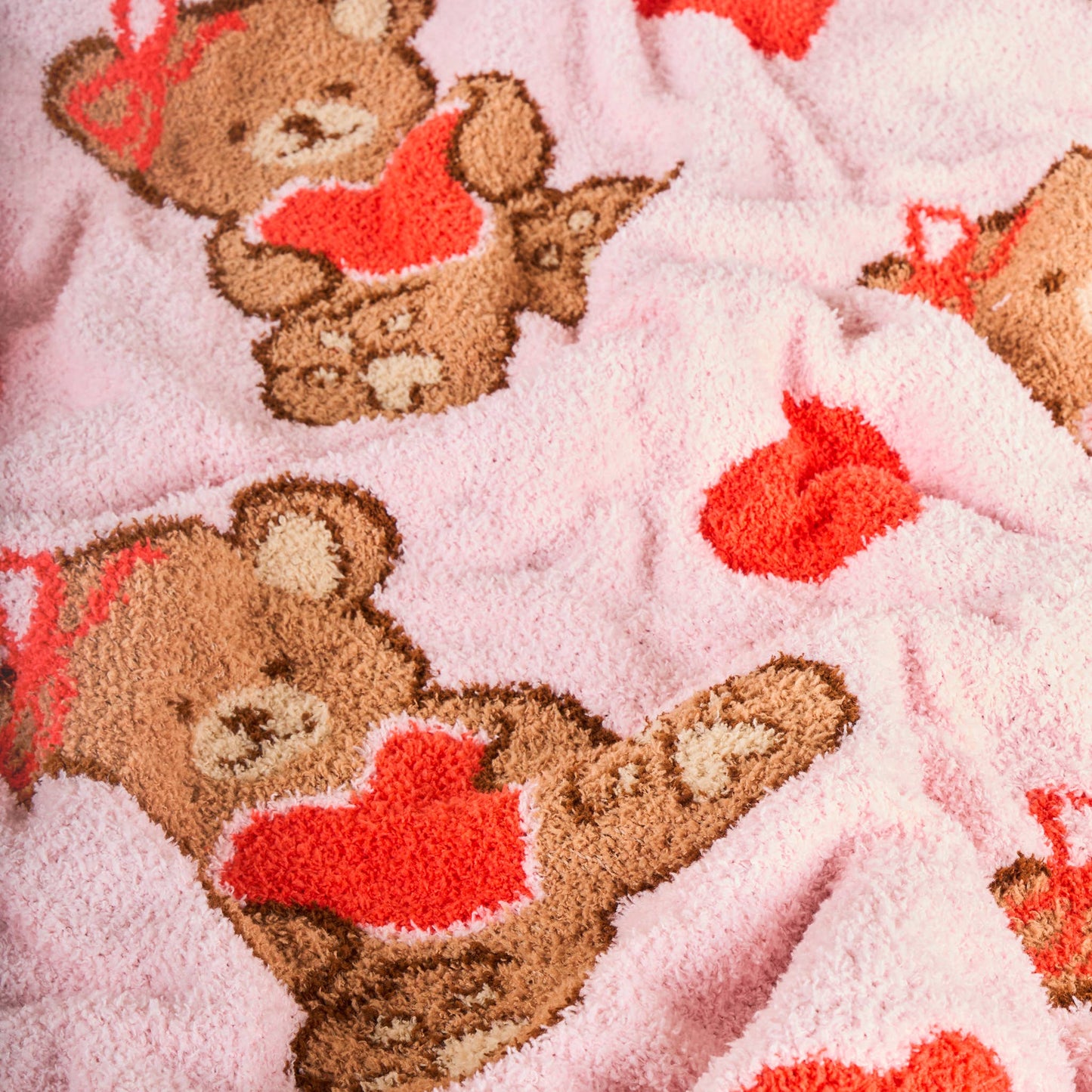 Cozy pink teddy bear blanket with heart patterns, soft plush material, perfect for cuddling.