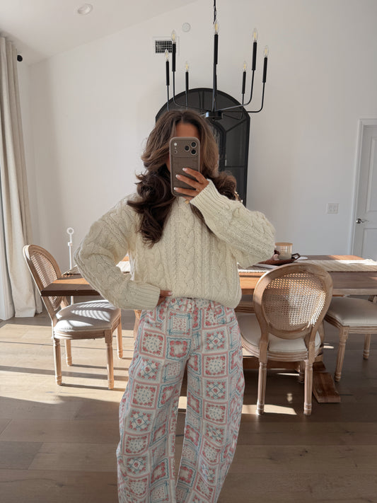 Cozy cream cable knit sweater paired with patterned wide-leg pants in pastel colors.