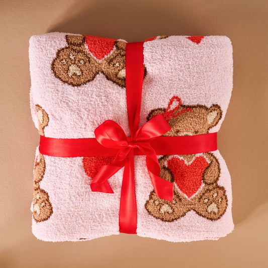 Cozy pink towel featuring teddy bear design, soft material, tied with a red ribbon, perfect for gifts.