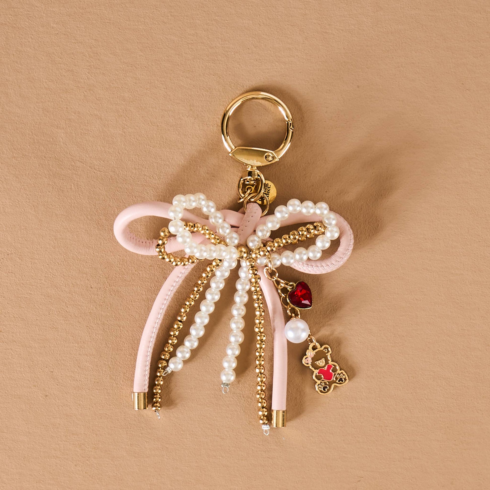 Pink bow keychain with pearls, gold accents, and a teddy bear charm for stylish accessorizing.