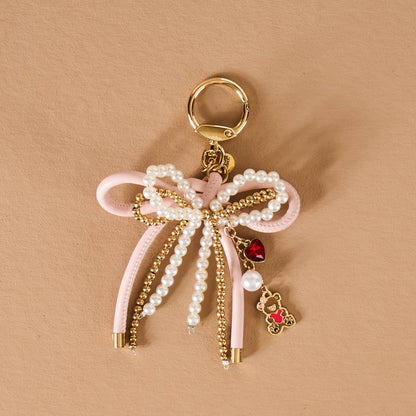Pink bow keychain with pearls, gold accents, and a teddy bear charm for stylish accessorizing.