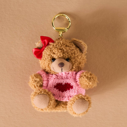 Cute plush teddy bear keychain with pink sweater and red bow, perfect for gifts and accessories.
