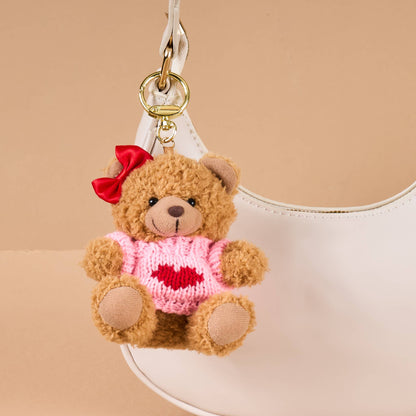 Cute plush teddy bear keychain in pink sweater with red heart and bow, perfect accessory for bags.